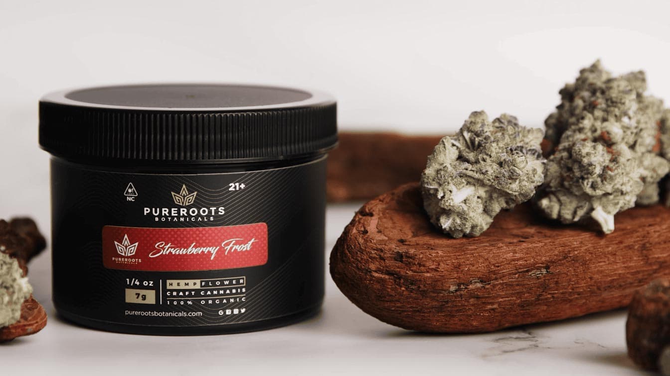 Pure Roots Botanicals Strawberry Frost THCA flower jar beside cured buds on a wooden slab